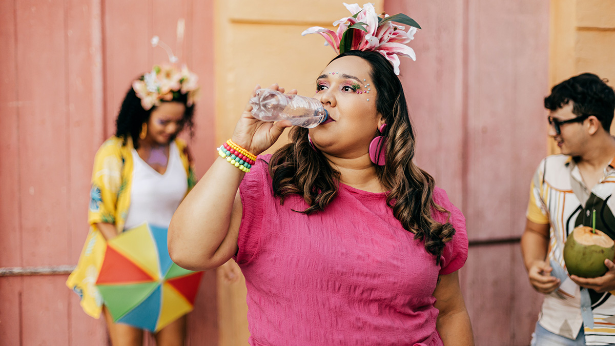 A curvy young woman in a pink shirt and a flower in her hair drinking water from a bottle at a summer party